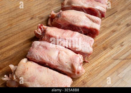 Una fila di dorsi di pollo crudi freschi tagliati a pezzi su un tagliere di legno. Primo piano, niente gente Foto Stock
