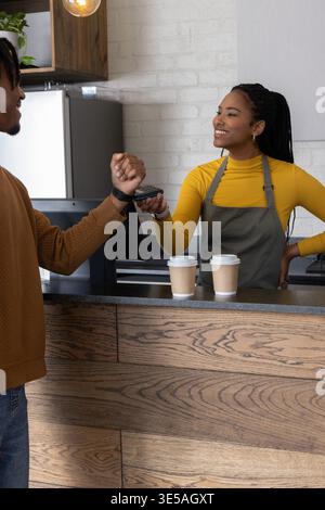 Barista afro-americano che serve il cliente al bar grembiule grigio con il lettore che tocca l'orologio Foto Stock