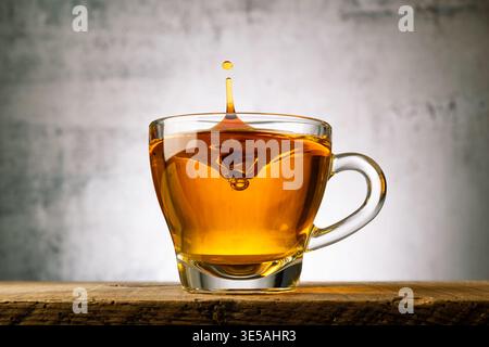 Tazza di tè in vetro su un tavolo di legno con gocce d'acqua. Foto Stock