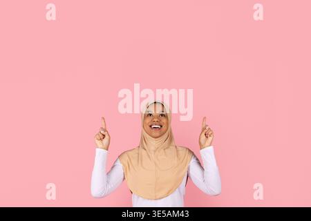 Giovane donna musulmana nera in hijab che punta entrambe le dita verso l'alto Foto Stock