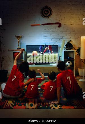La famiglia guarda la partita di calcio in TV a casa e tifa per il gol insieme. Foto Stock