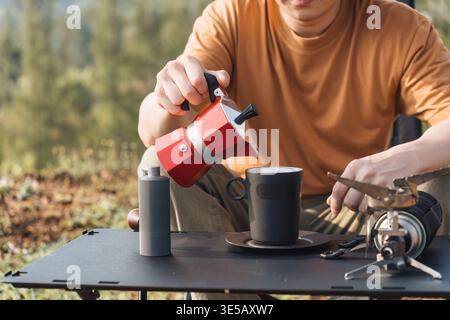 Primo piano che versa caffè dalla moka in una tazza mentre campeggi nella natura all'aperto Foto Stock