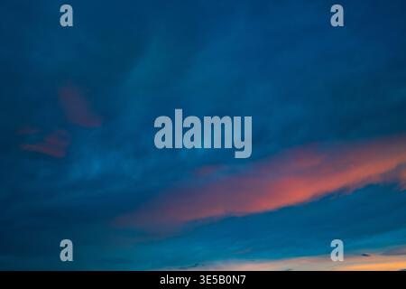 Il cielo al crepuscolo mostra nuvole blu profonde striate di calde tonalità rosa e arancione. I colori si fondono delicatamente all'orizzonte. L'umore è calmo e sereno, perfetto Foto Stock