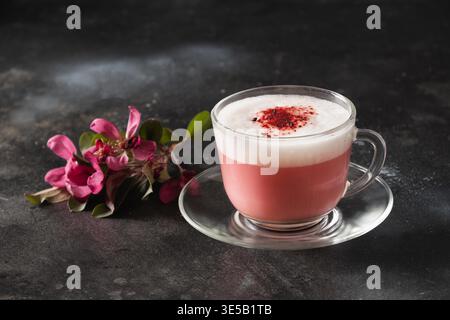 Latte matcha rosa con fiori sakura decorati a polvere su sfondo nero. Bevanda vegana alternativa alla moda. Primo piano. Foto Stock