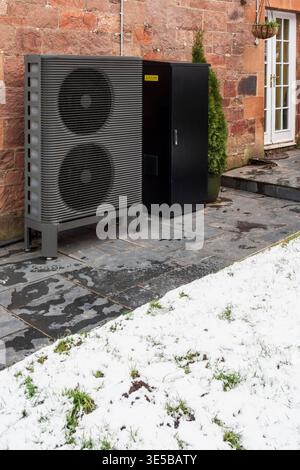 Una pompa di calore a sorgente d'aria e batterie di stoccaggio fuori da una vecchia casa in pietra in Scozia in inverno con neve Foto Stock