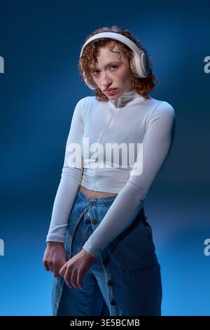 Una giovane donna con vivaci ricci rossi ama i suoi brani preferiti in un'accogliente atmosfera da studio. Foto Stock