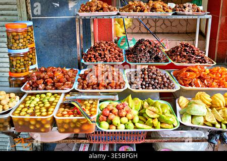 I venditori locali vendono vari tipi di frutta e spuntini in un affollato mercato di Hanoi. I colori e le forme attraggono molti clienti nelle vicinanze. Foto Stock