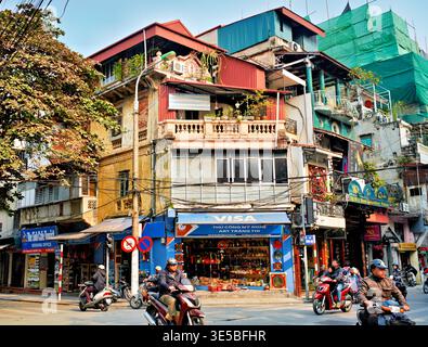 Le motociclette attraversano le strade trafficate di Hanoi. I negozi fiancheggiano la strada con cartelli colorati ed edifici. La gente si occupa della propria vita quotidiana. Foto Stock