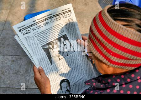 Una persona anziana tiene un giornale mentre è seduta fuori ad Hanoi. La scena cattura la vita quotidiana in Vietnam durante il giorno. Foto Stock