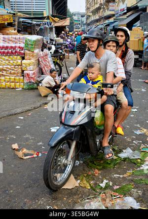 Una famiglia guida in moto attraverso una strada affollata nella città di ho chi Minh. La scena mostra negozi, persone e disordine nelle strade. Foto Stock