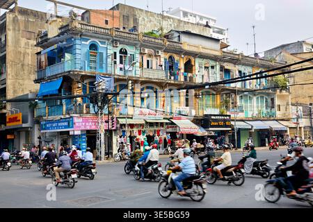 Le moto si muovono attraverso una strada trafficata di ho chi Minh City. I negozi espongono merci e la lavanderia è appesa ai balconi. Foto Stock