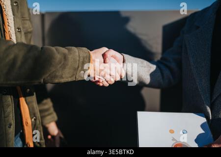 Stretta di mano tra due professionisti su documenti durante una riunione all'aperto, primo piano di mani Foto Stock