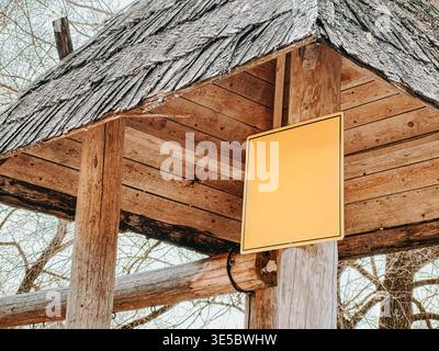 Cartello giallo vuoto montato su un rustico riparo in legno con tegole intemprate. Ideale per modelli pubblicitari, concetti di wayfinding, turismo rurale, Foto Stock