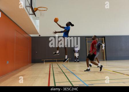 Diversi giocatori maschili di abbigliamento sportivo che giocano a basket in palestra, saltano a strapiombo verso il cerchio Foto Stock