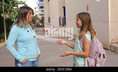 La madre premurosa con cappuccio azzurro ascolta attentamente la figlia sorridente Foto Stock