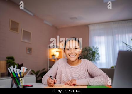 Ragazza sorridente mentre fa i compiti a casa Foto Stock