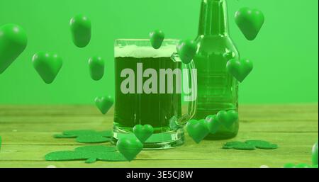 Tazza di vetro con birra verde, schiuma su piano in legno con bottiglia verde, shamrock, cuori Foto Stock