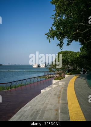 Wuhan, Cina - 16 giugno 2025: Lungomare lastricato curvo con pavimentazione tattile gialla per i non vedenti e un ponte inferiore in legno con Foto Stock