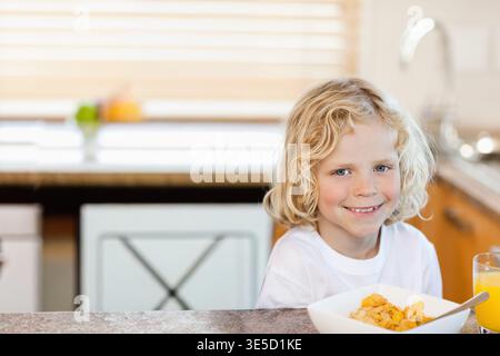 Ciotola per cereali seduta sul bancone della cucina accanto al bicchiere di succo d'arancia, lavare il rubinetto con il luccichio. Colazione, bambino, mattina, luce del giorno, casa, finestra, tapparelle Foto Stock