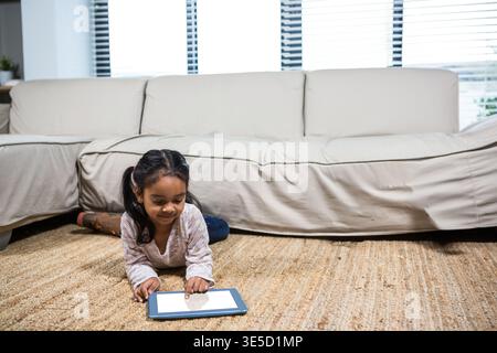 Tablet che mostra contenuti e si appoggia su un tappeto in tessuto beige vicino a un divano color crema e alle tende da finestra. Bambini, tempo libero, accogliente, minimalismo, domestico, rel Foto Stock