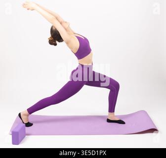 Giovane donna in abbigliamento sportivo viola che fa un affondo per yoga Foto Stock