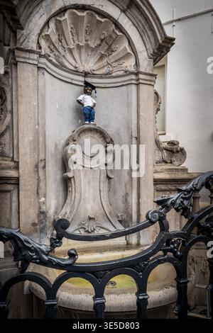Un primo piano della famosa statua di Manneken Pis a Bruxelles, vestito con un abito graduato con una camicia bianca, pantaloni blu e un mortarboard. Il fratello Foto Stock
