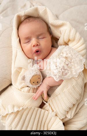 Tenero bambino appena nato che sbadiglia durante il sonno, avvolto in morbido tessuto lavorato a maglia. Fotografia naturale del neonato che cattura la tenerezza, la calma e la prima infanzia Foto Stock