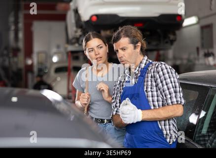 Lavoratore di officina di riparazione auto maschile che consulta cliente donna Foto Stock
