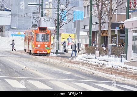 Una pittoresca scena stradale invernale a Sapporo, Hokkaido. Un tram d'epoca arancione corre lungo le piste innevate, creando un m nostalgico e romantico Foto Stock