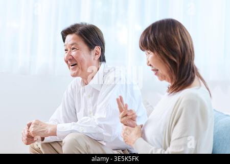 Una coppia giapponese sorridente che fa una piacevole conversazione nel salotto di casa Foto Stock