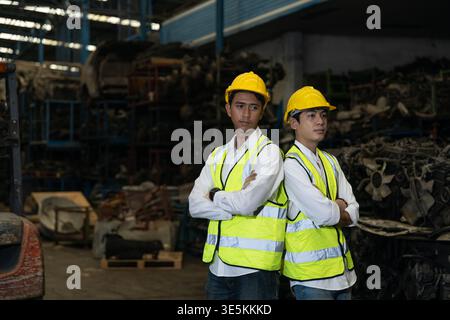 Due lavoratori industriali asiatici sicuri che si mettono dietro in magazzino indossando gli attrezzi di sicurezza Foto Stock