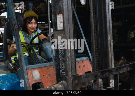 Operatore di carrelli elevatori a forche che lavora in magazzino indossando casco e giubbotto di sicurezza Foto Stock