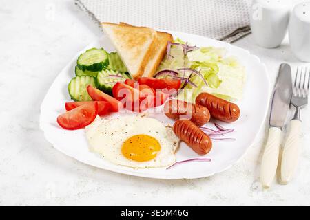 Colazione salutare. Uova fritte, salsicce, pane tostato e verdure fresche. Foto Stock