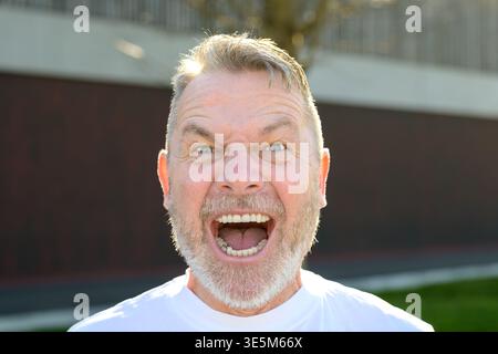 Ritratto espressivo di un uomo maturo che urla a bocca aperta nella luce naturale del sole. Foto Stock