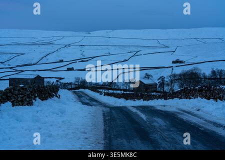 Strada di campagna che passa attraverso campi innevati e fienili di pietra a Swaledale Foto Stock