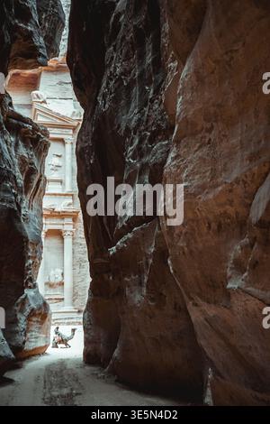 Vista della facciata del Tesoro di Petra Treasury, vista attraverso lo stretto canyon di arenaria con cammello in primo piano Foto Stock