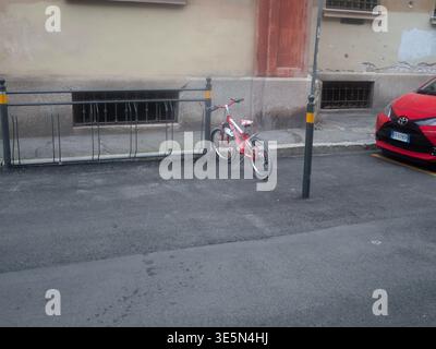 Lombardia, Italia - 15 marzo 2026 la bicicletta bianca e rossa di Legnano è parcheggiata accanto ad un portapacchi in metallo nero su una strada urbana asfaltata, con un'auto rossa visibile Foto Stock