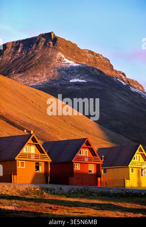 Case colorate sorgono accanto a una montagna durante il tramonto a Longyearbyen, Svalbard. La luce proietta lunghe ombre sul terreno. Foto Stock