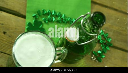 Tazza da birra in vetro che si schiude su un tavolo in legno accanto alla bottiglia verde di shamrock garland, copia spazio Foto Stock