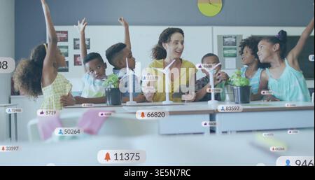Tenendo in mano un tablet, l'insegnante indossa la parte superiore gialla e guida i bambini in classe con le sovrapposizioni delle turbine eoliche Foto Stock