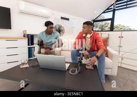 Diversi amici maschi registrano podcast in un luminoso studio attico, con laptop e microfoni Foto Stock