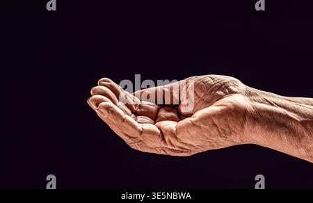 Signora anziana sta aspettando aiuto. Mano che il palmo si allontana in avanti. Mano vecchio su sfondo nero. La mano di una vecchia signora con il palmo aperto Foto Stock