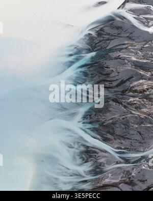 Vista aerea dei fiumi glaciali che scavano sentieri attraverso terreni accidentati, contrastando il blu gelido con il paesaggio roccioso, il lago Tekapo, Canterbury Reg Foto Stock