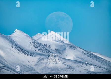 Luna piena che sorge al crepuscolo sulle cime innevate dell'Islanda Foto Stock
