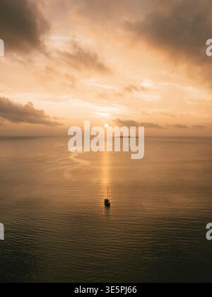Vista aerea di una barca solitaria che naviga sul tranquillo e dorato mare sotto un cielo caldo e nuvoloso, Pine Island, l'Île-des-Pins, nuova Caledonia. Foto Stock