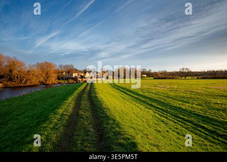 Il sole serale invernale illumina un argine di difesa alimentare accanto a un fiume con case sulla riva lontana, Doncaster, South Yorkshire. Foto Stock