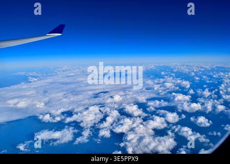 Una vista aerea mozzafiato attraverso la finestra di un aereo, che cattura il cielo blu profondo che si fonde con l'orizzonte terrestre durante un volo a lungo raggio Foto Stock
