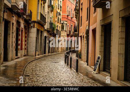 La piovosa strada acciottolata nella storica città vecchia di Girona, Catalogna, Spagna, con colorati edifici mediterranei e riflessi sulla pavimentazione bagnata. Foto Stock