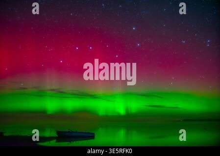 splendida aurora boreale verde rossa sul lago in autunno con una barca solitaria Foto Stock