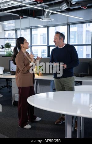 Colleghi diversi in piedi e che parlano in un ufficio open space, donna in blazer, uomo in possesso di un tablet Foto Stock